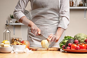 The chef cooks, cuts an apple, in the process of a vegetarian salad with the hand of the chef in the home kitchen. Light
