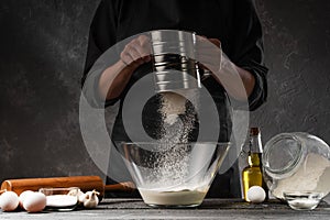 Chef cooks dough. With flour frozen in motion. Against the background of ingredients. Cooking flour products, bread, Italian pasta