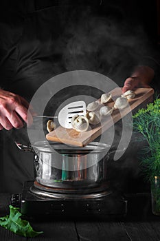 The chef cooks dumplings in a saucepan in the restaurant kitchen. Close-up of the hands of the cook during work