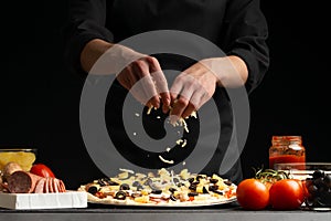 The chef cooks Italian pizza, sprinkles with mozzarella cheese. Freeze in motion. Against the background of pizza ingredients.