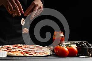 Chef cooks Italian pizza, sprinkles with mushrooms. Freeze in motion. Against the background of pizza ingredients. Black