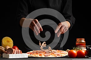 Chef cooks Italian pizza, sprinkles with mushrooms. Freezing in motion. Against the background of pizza ingredients. Black