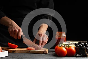 Chef cooks pizza, slices fresh tomatoes, on the background with ingredients. Recipe book, menu, home cooking. close-up