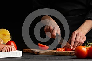 Chef cooks pizza, slices fresh tomatoes, on the background with ingredients. Recipe book, menu, home cooking. close-up