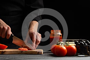 Chef cooks pizza, slices fresh tomatoes, on the background with ingredients. Recipe book, menu, home cooking. Horizontal frame