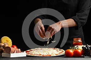 Chef cooks pizza, sprinkled with mozzarella cheese, freezing in motion on the background with ingredients. Recipe book, menu, home