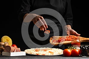 The chef cooks pizza, sprinkles fresh tomatoes, on a background with ingredients. Recipe book, menu, home cooking