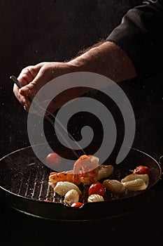 Chef cooks seafood, shrimp in a pan with vegetables.