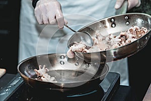 The chef cooks the small octopus on a metal frying pan