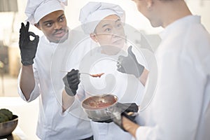 Chef cooks tasting sauce with a spoon while cooking in the kitchen