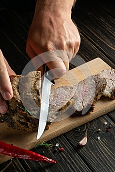 The chef cuts the baked veal meat with a knife for cooking dinner in the kitchen. Fast street food concept on dark background