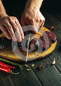 The chef cuts blood sausage on a kitchen cutting board with a knife. Cooking a national dish with spices and peppers in the