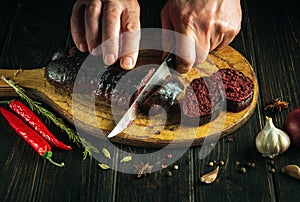 The chef cuts blood sausage on a kitchen cutting board with a knife in his hand. The concept of cooking a national dish with