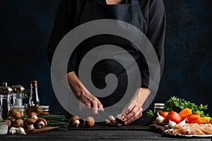 Chef cuts with knife champignons on the table with variety ingredients for cooking mushroom pie on dark blue background. Concept