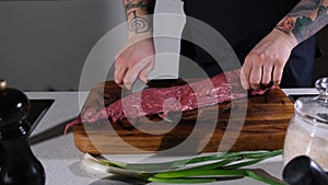 the chef cuts the meat on a wooden chopping board, preparing it for further cooking. The cook cuts out the excess parts