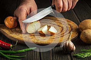 Chef cuts onion with a knife on a cutting board for making soup for lunch. Vegetable diet idea. Peasant food