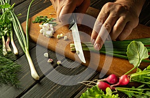 The chef cuts the onion with a knife on the kitchen cutting board. Vegetarian products or fresh vegetables on the kitchen table