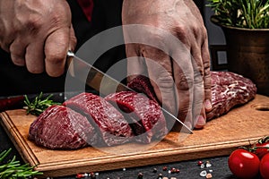 The chef cuts a piece of veal beef meat on a dark background, Whole piece of tenderloin with steaks and spices ready to cook