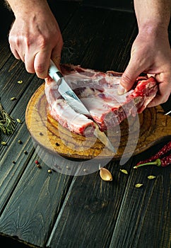 The chef cuts raw ribs with a knife on a cutting board before preparing a meat dish. Recipe idea for a hotel