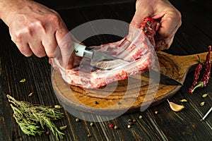 The chef cuts raw ribs with a knife on a wooden board. The concept of the process of preparing a meat dish. Asian cuisine
