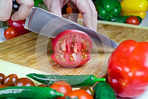 Chef cuts tomatoes into pieces on a cutting Board with a sharp cooking knife