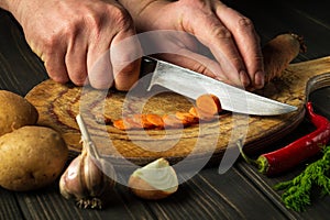 Chef is cutting carrots for vegetable soup in the restaurant kitchen. Close-up of the hands of the cook during work. Carrot diet