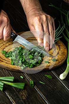 Chef cutting green onion on a cutting board with a knife for preparing a vegetarian dish. Peasant food
