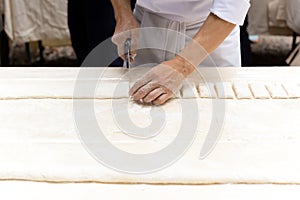 Chef cutting a pastry dough with pizza knife on table top.