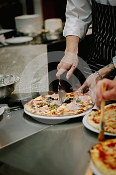 Chef cutting pizza with the round pizza cutter or knife.