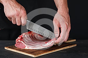 Chef cutting rack of lamb on wooden board in kitchen