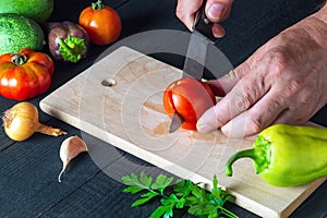 Chef is cutting a red tomato in a restaurant kitchen, a for a salad. Close-up of the hands of the cook during work on table