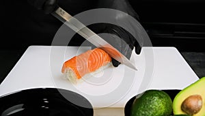 Chef cutting rolls of sushi with a knife on a white board.