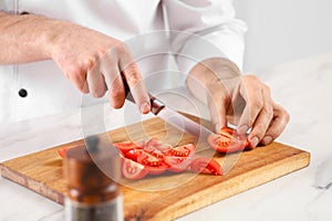 Chef cutting tomatoes at marble table in kitchen, closeup