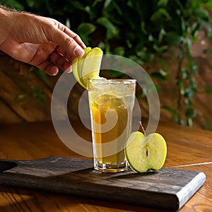 Chef decorates apple juice or drink glass with green apple slices. Male hand in Cooking process of fruit refreshing