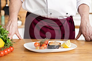 Chef with diligence finishing dish on plate, fish with vegetables