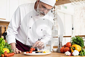 Chef with diligence finishing dish on plate, fish with vegetables