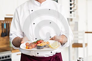 Chef with diligence finishing dish on plate, fish with vegetables