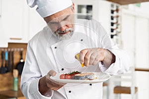 Chef with diligence finishing dish on plate, fish with vegetables