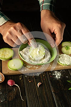 The chef dusts the sliced zucchini with flour before roasting. The concept of cooking vegetable marrow on the kitchen table with