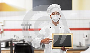 Chef in face mask with chalkboard at kitchen