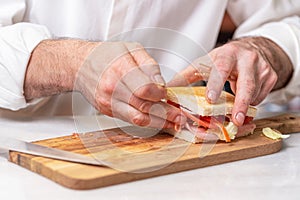 Chef finalizes the sandwich with ham and salad on the wooden board. photo
