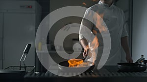 Chef fires up the flambe on a hot pan at the kitchen in slow motion, big open fire in the kitchen, pan on fire, cooking