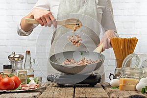 Chef fries bacon, meat in a frying pan on the background of a light kitchen. Culinary recipes, cooking