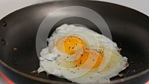 A chef fries an egg, sunny side up, in a small frying pan over industrial gas burning stove with a shallow depth of