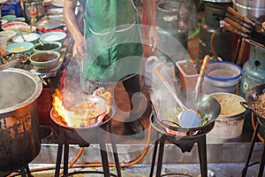 Chef fries in wok on vast flame of stove with rising steam at street cafe in Chinatown of Bangkok, Thailand