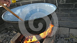 Chef is frying chopped onion in deep pod above open grill fire. Preparation of traditional goulash for family and friends party