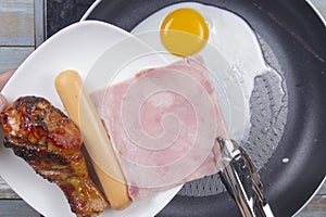 Chef frying egg ,ham,sausage and chicken drumstick in the pan