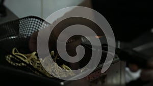 Chef frying food in flaming pan on gas hob in commercial kitchen.