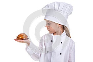 Chef girl in a cap cook uniform, holding the bun in the right hand. Looking at the bun