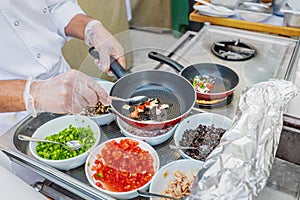 Chef gloved hands cook vegetables and other ingredients on a gas stove in frying pan